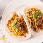 two shredded chicken tacos recipe on a round white plate with guacamole on top.