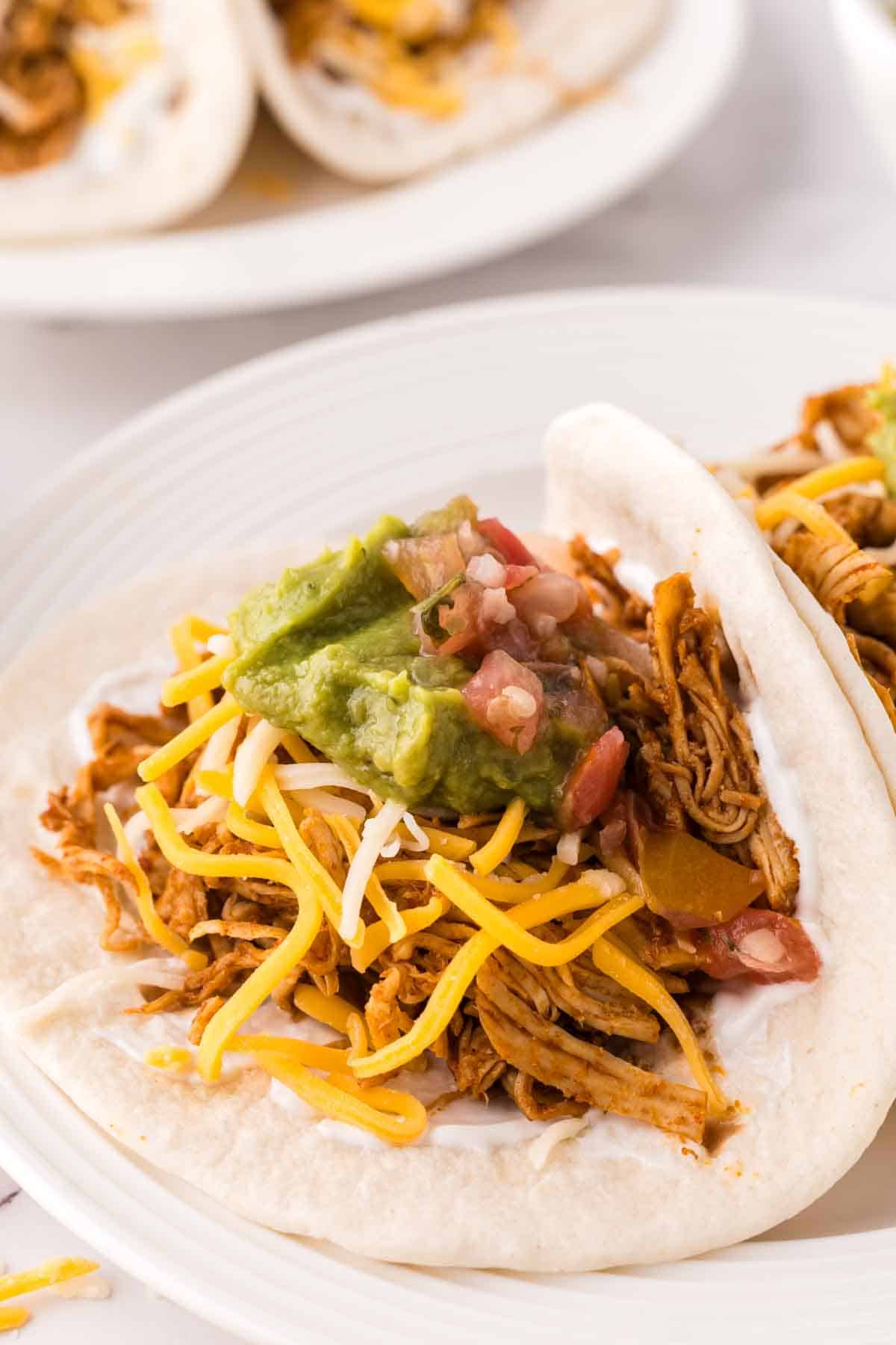 two shredded chicken tacos recipe on a round white plate with guacamole on top.