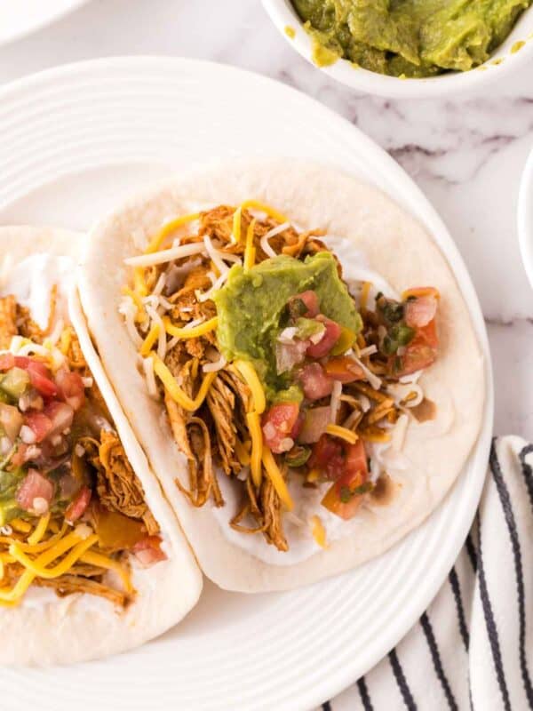 two shredded chicken tacos recipe on a round white plate with guacamole on top.