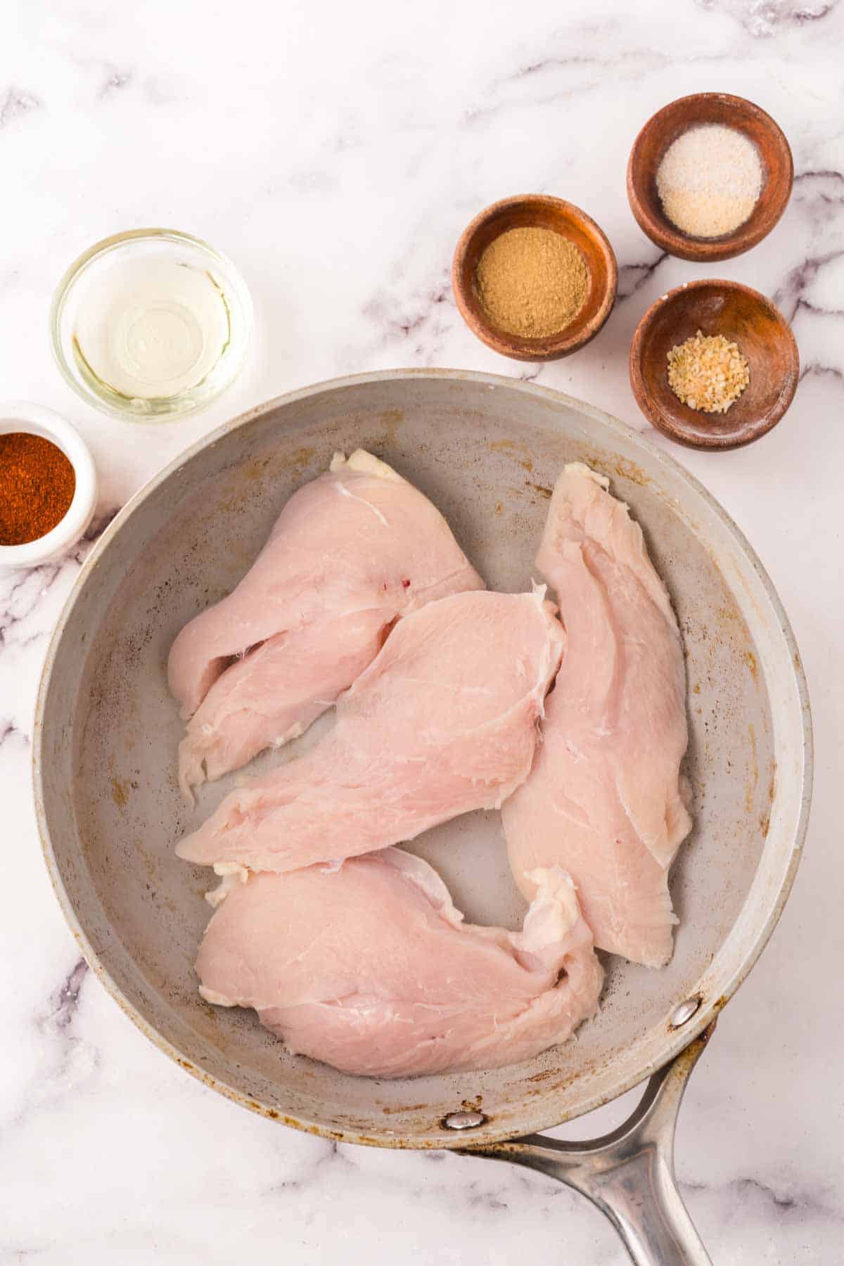 a pan of four raw chicken breasts ready to cook.