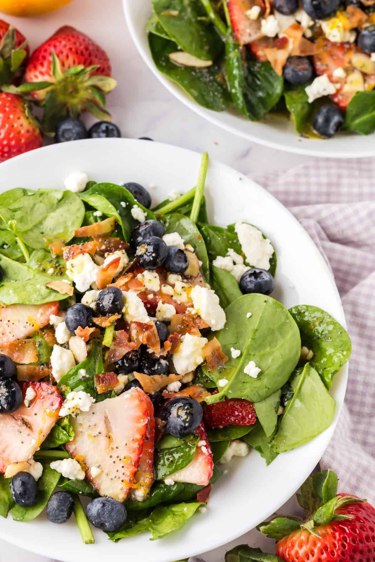 spinach and berry salad on a round white plate with black forks to the side.