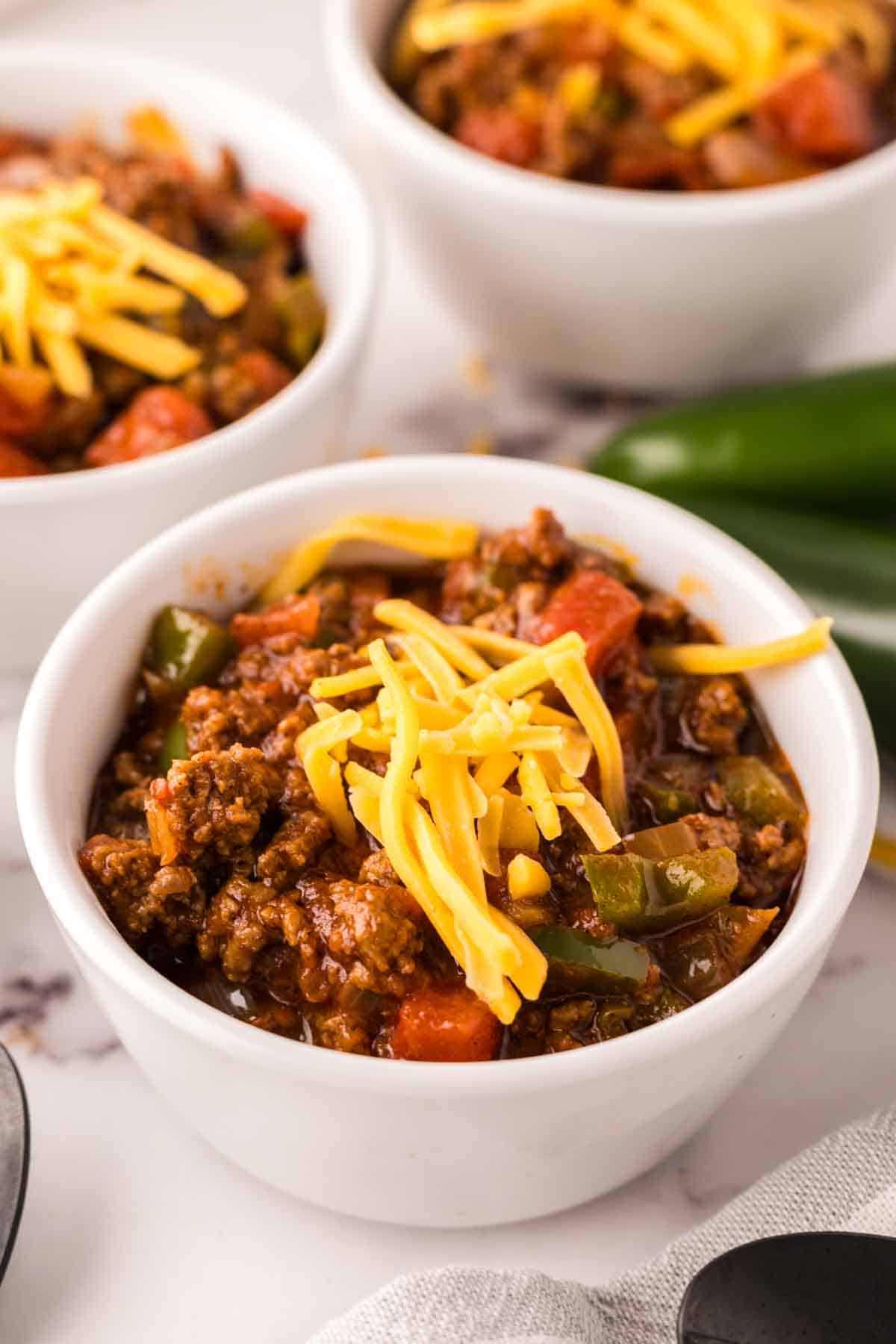 small bowl of texas chili with shredded cheese on top and jalapeños around.