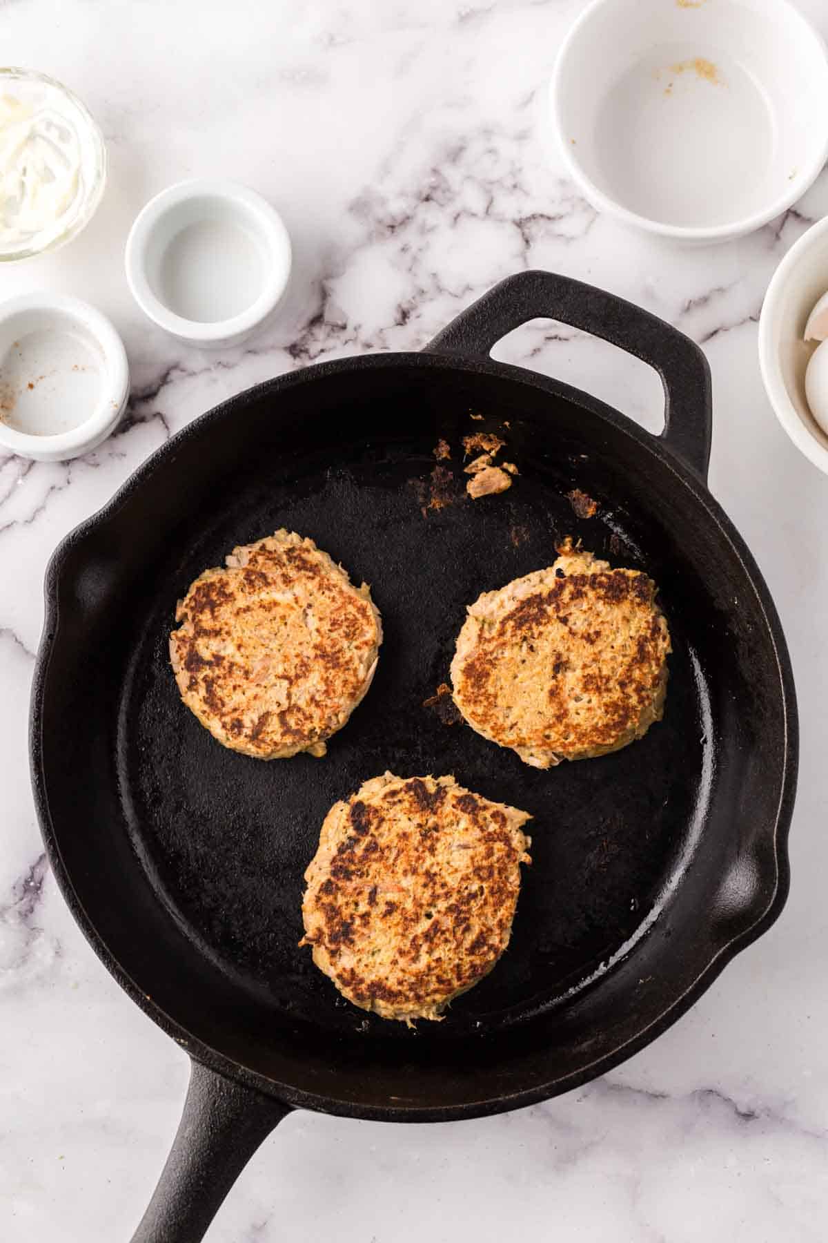 cast iron skillet with three tuna patties cooking.