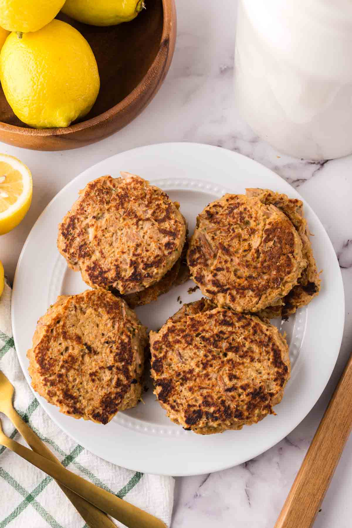 four tuna patties on a round white plate with lemons to the side.