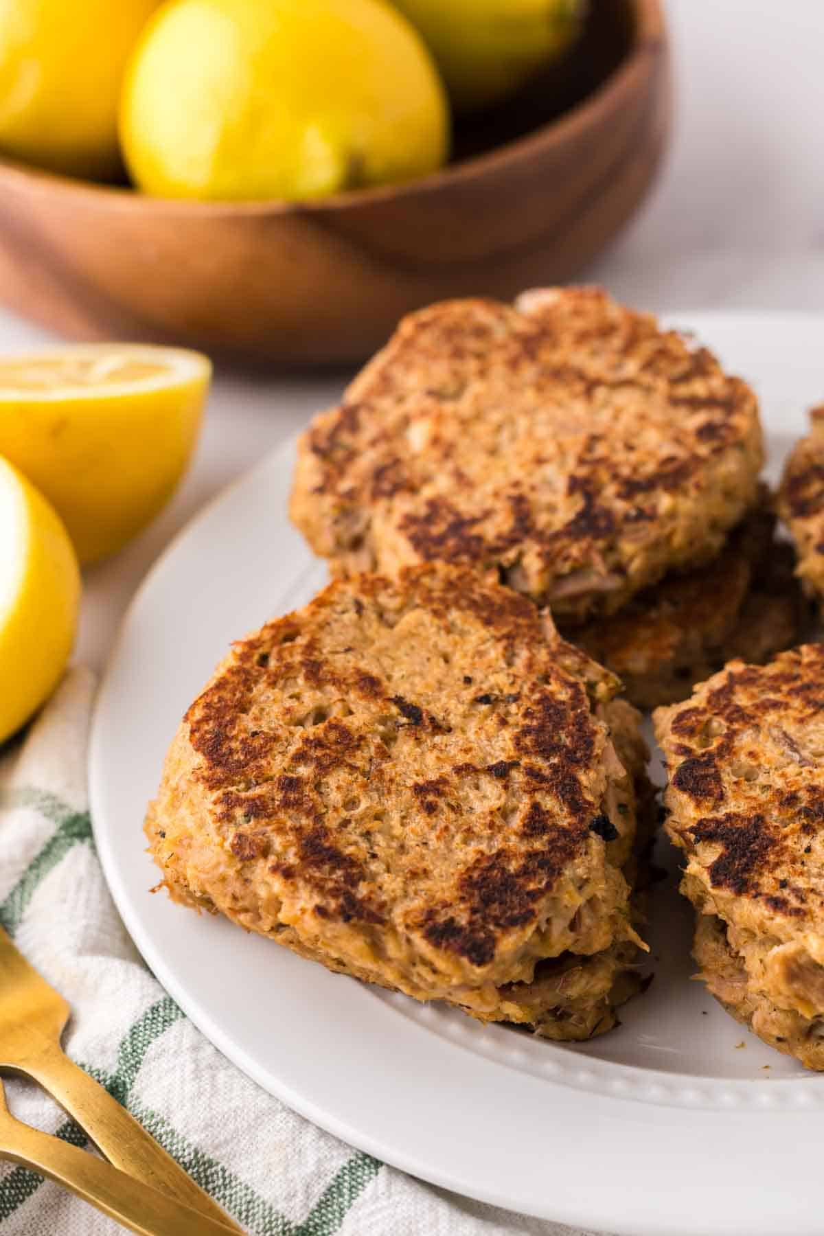 four tuna patties on a round white plate with lemons to the side.