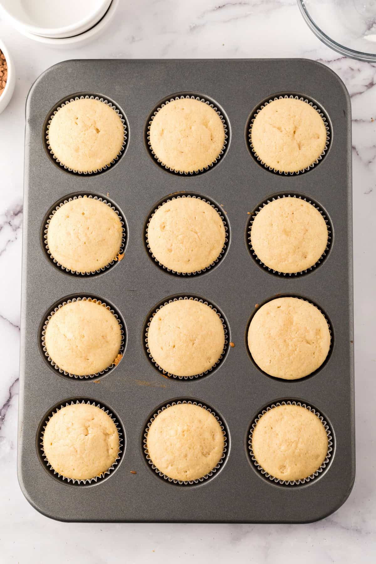 12 freshly baked vanilla cupcakes in the tin.