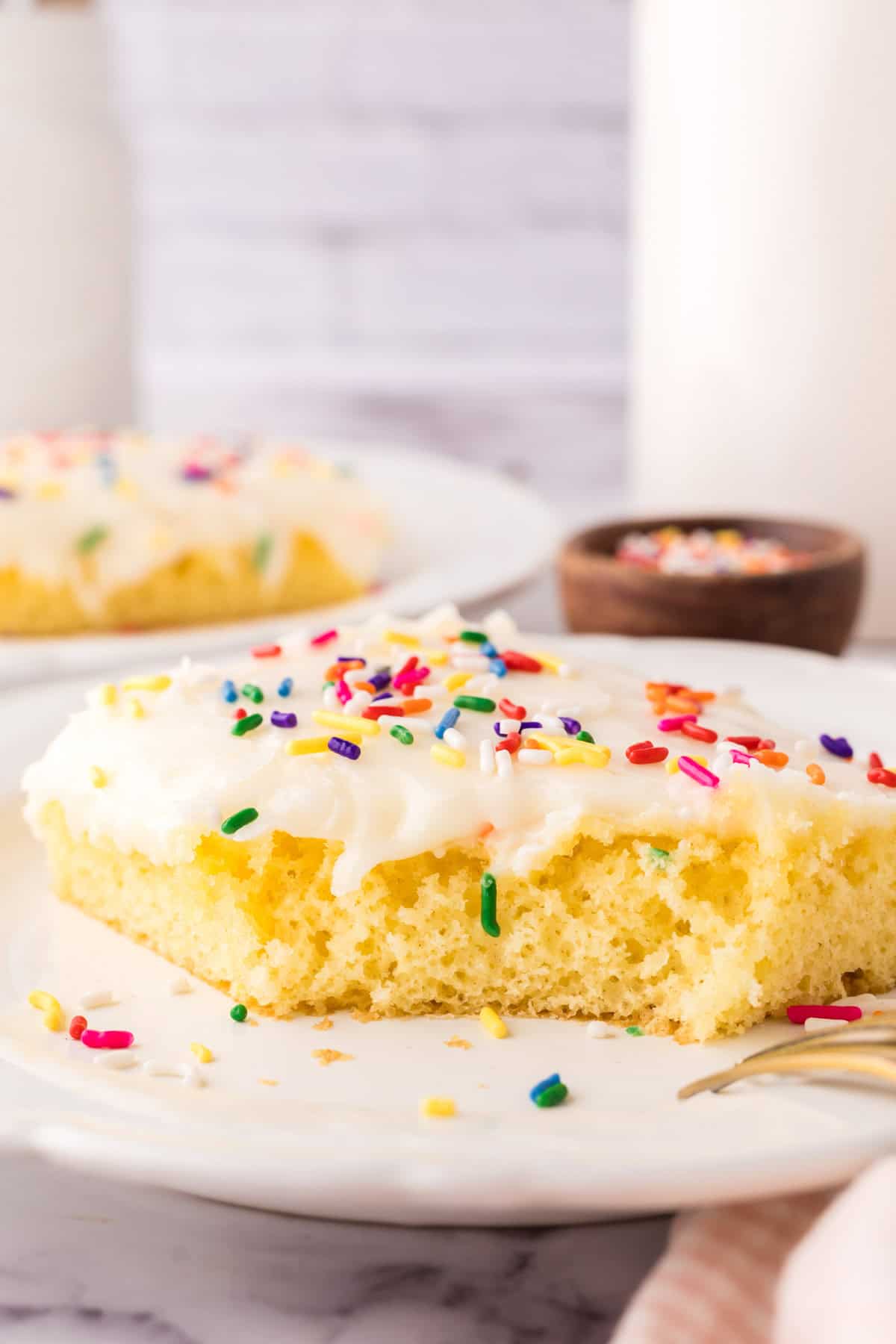 vanilla sheet cake with rainbow sprinkles and a bite taken out.