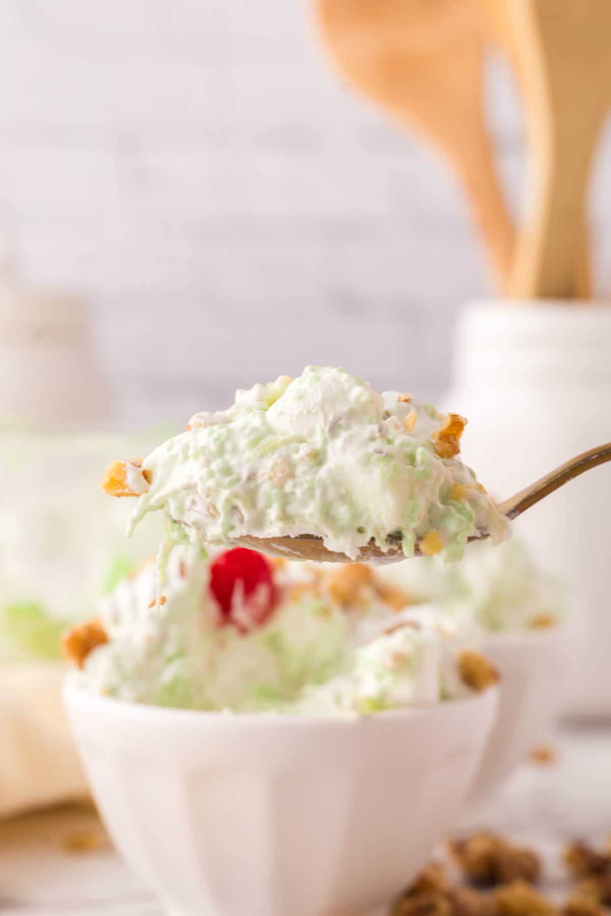 spoonful watergate salad over the small bowl with nuts and a cherry on top.