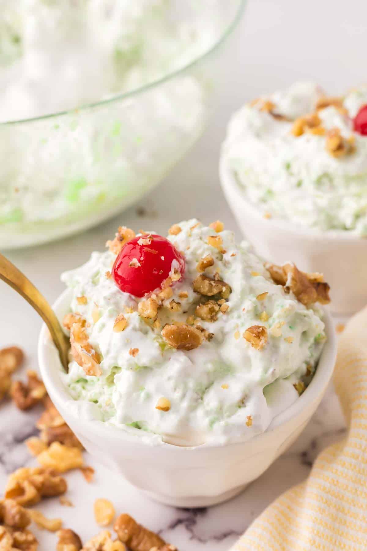 spoonful watergate salad over the small bowl with nuts and a cherry on top.