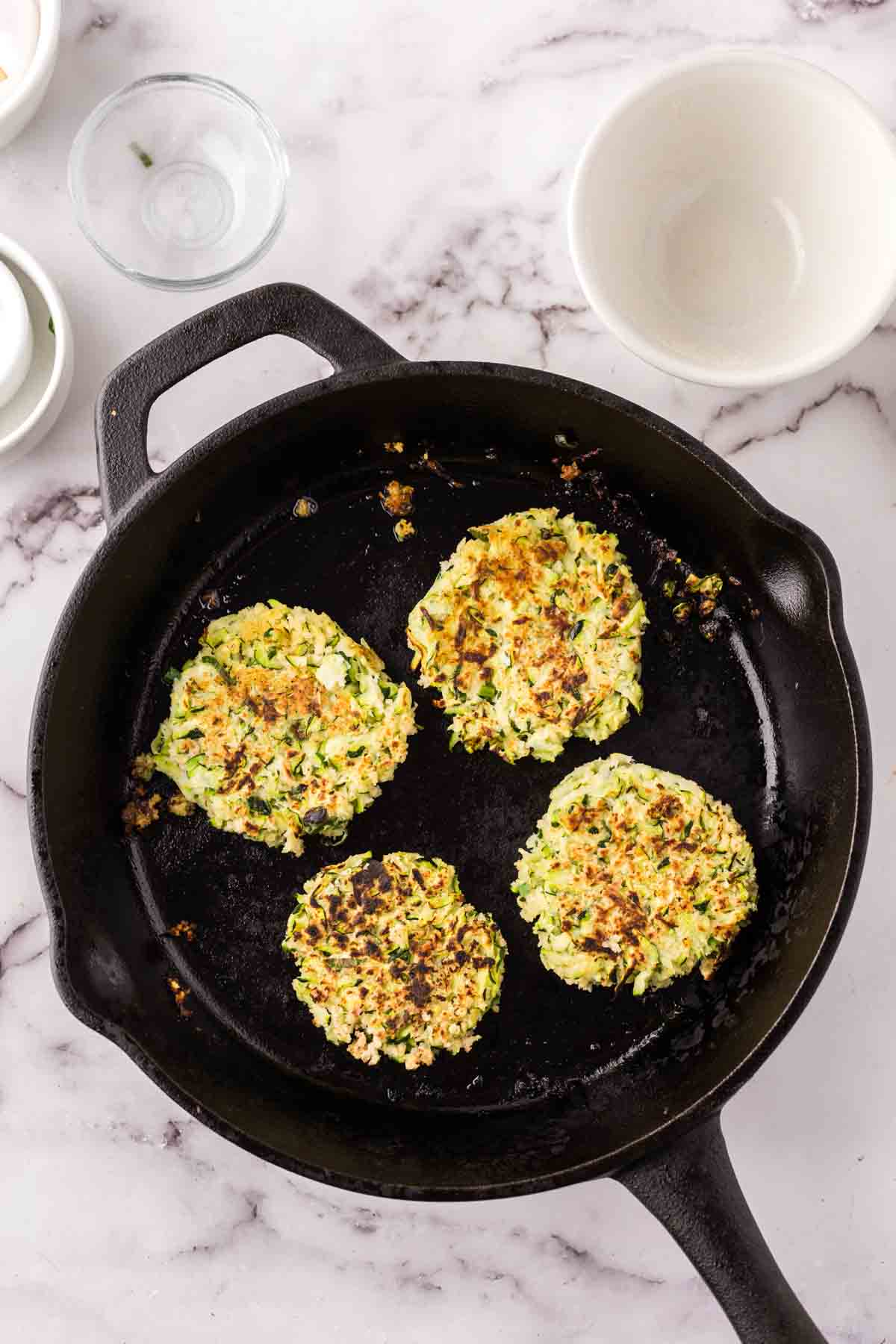 cast iron skillet with frou-frou zucchini fritters cooking.