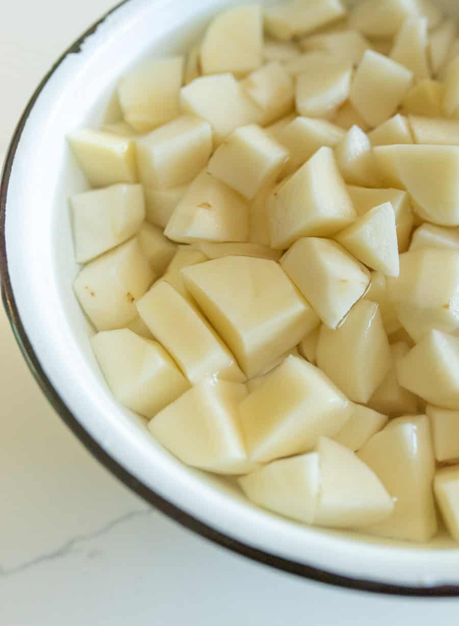 Raw potato cubes soaking in water in a white enamel bowl with a black rim.
