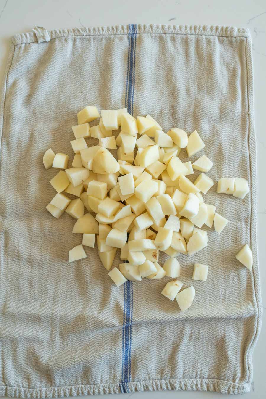 Raw potato cubes on a light grey towel after being dried. 