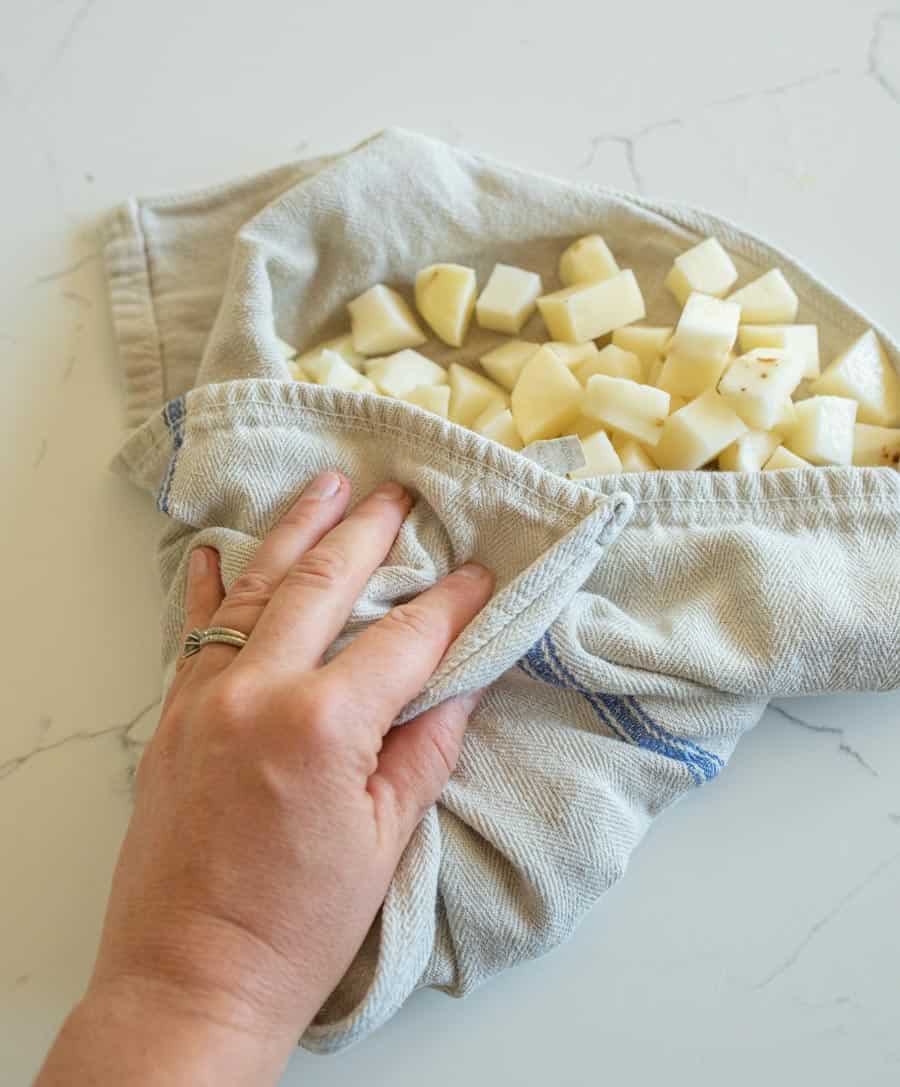 Raw potato cubes being dried in a light grey towel.