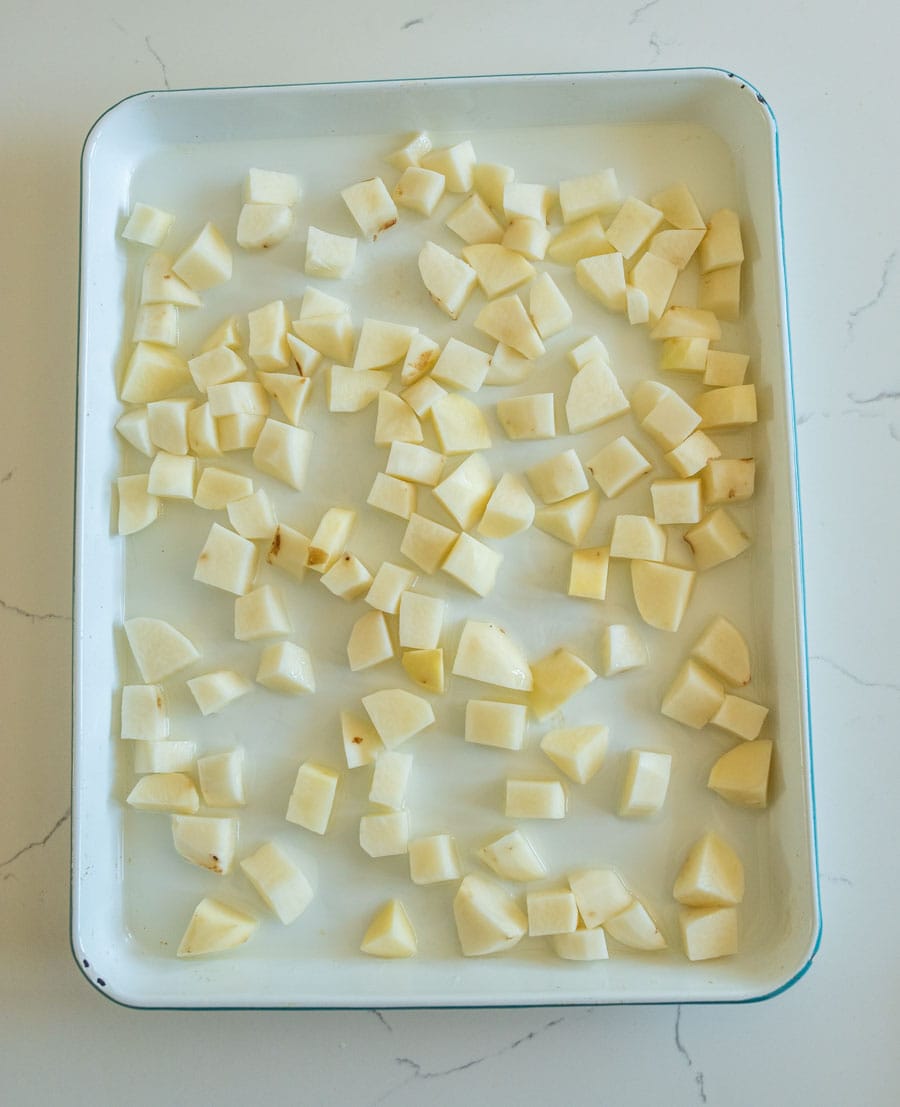 Raw potato cubes on a white enamel sheet pan.