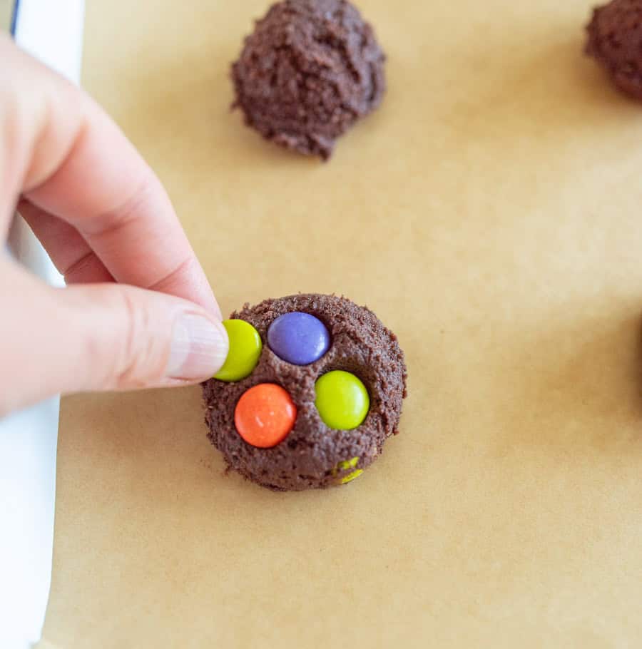 Dark chocolate cookie dough ball with a hand pushing in M&M candies.