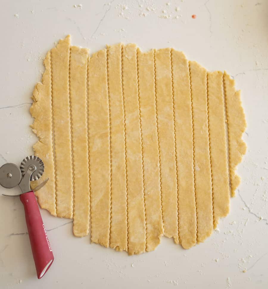 The second pie crust cut into one-inch strips and a pastry cutter on a lightly floured white counter. 