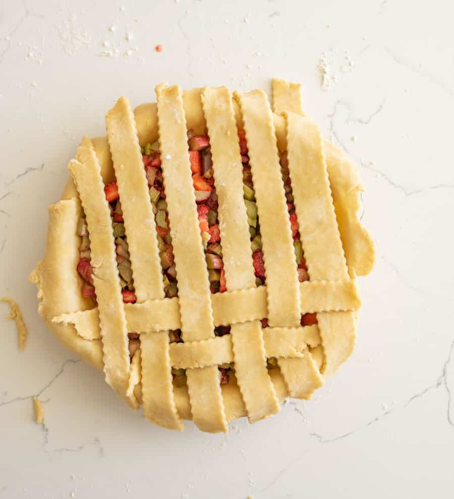 A second strip of pie crust has been added to the pie and all strips are resting down on the pie. 