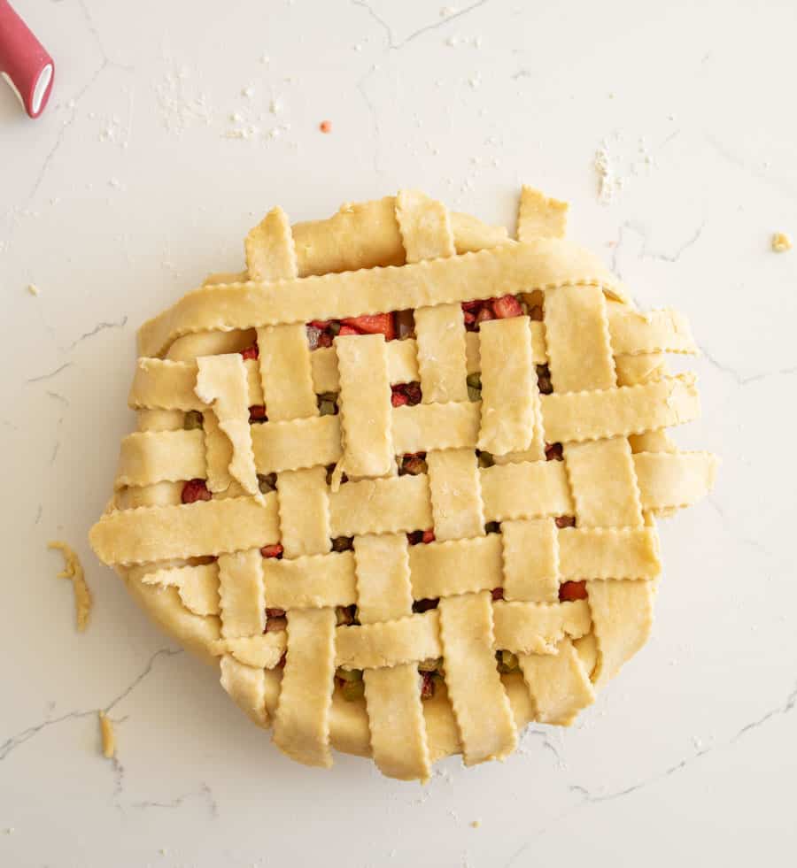 Three strips of pie crust are folded back and the last strip of pie crust is resting perpendicular to the folded back strips. 