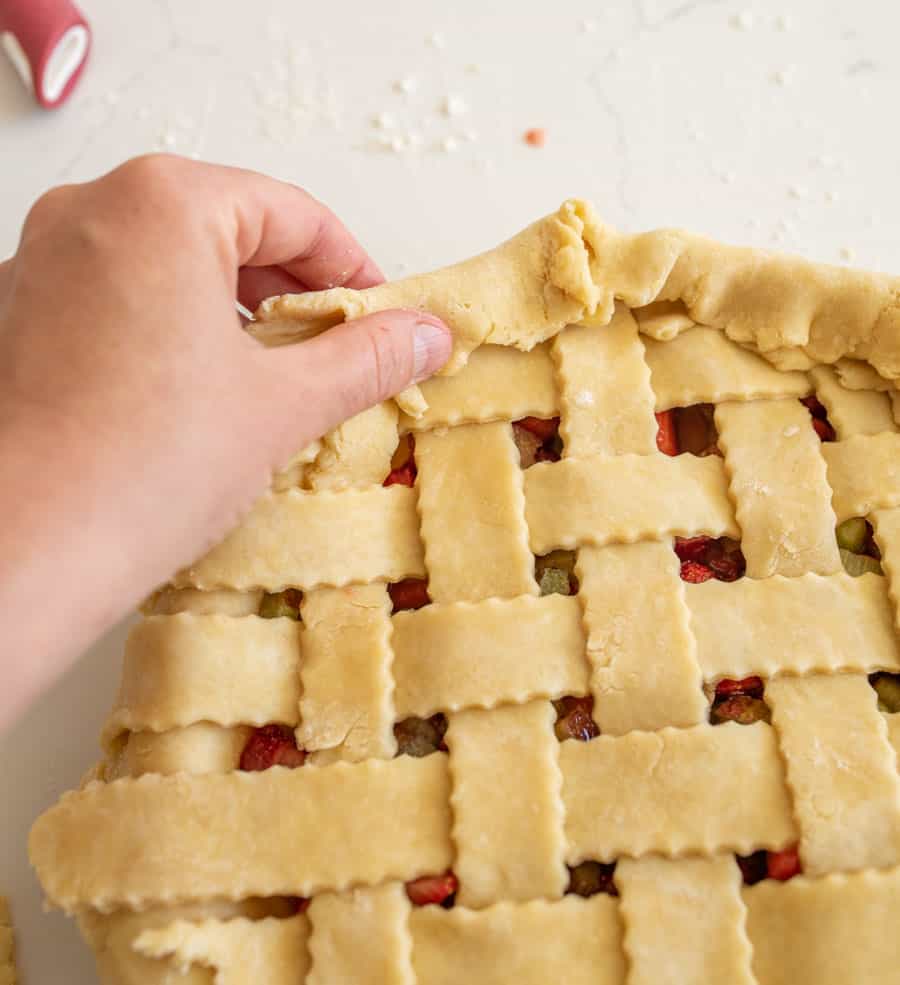 A hand folding the bottom piece of pie crust over the lattice top.