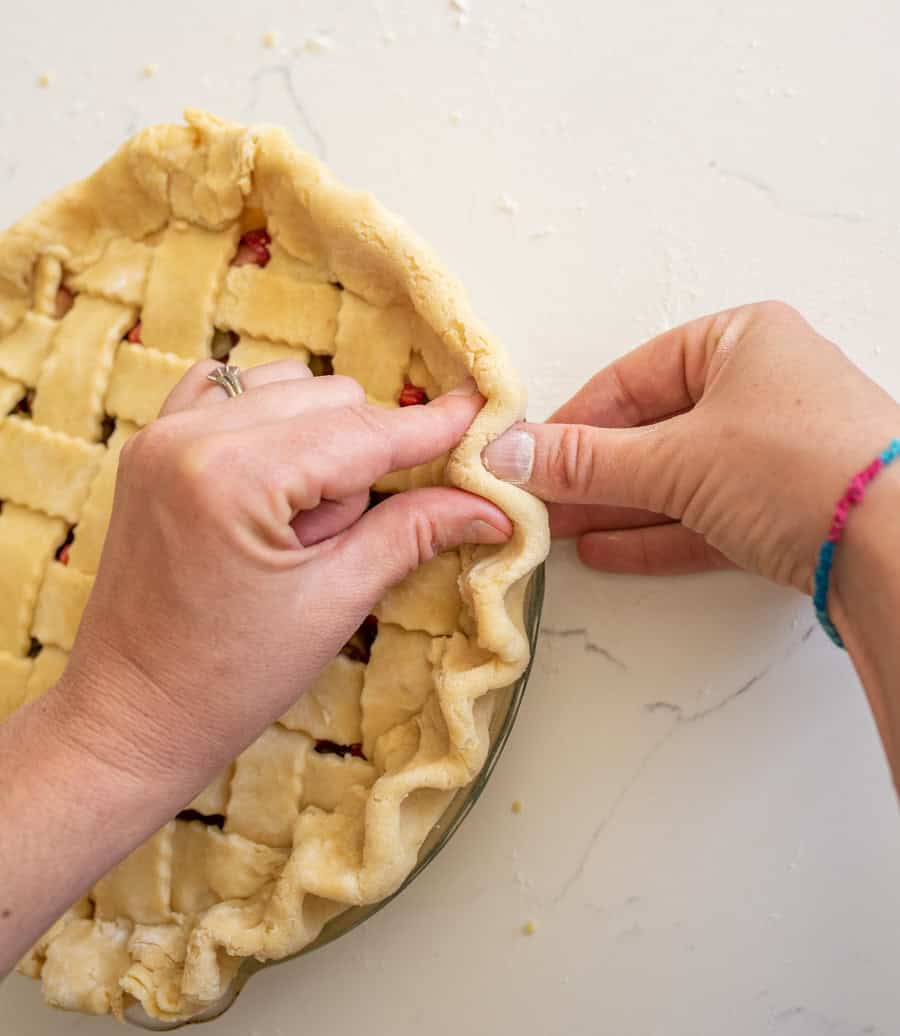 Two hands pinching the two layers of pie crust around the edge of the pie. 