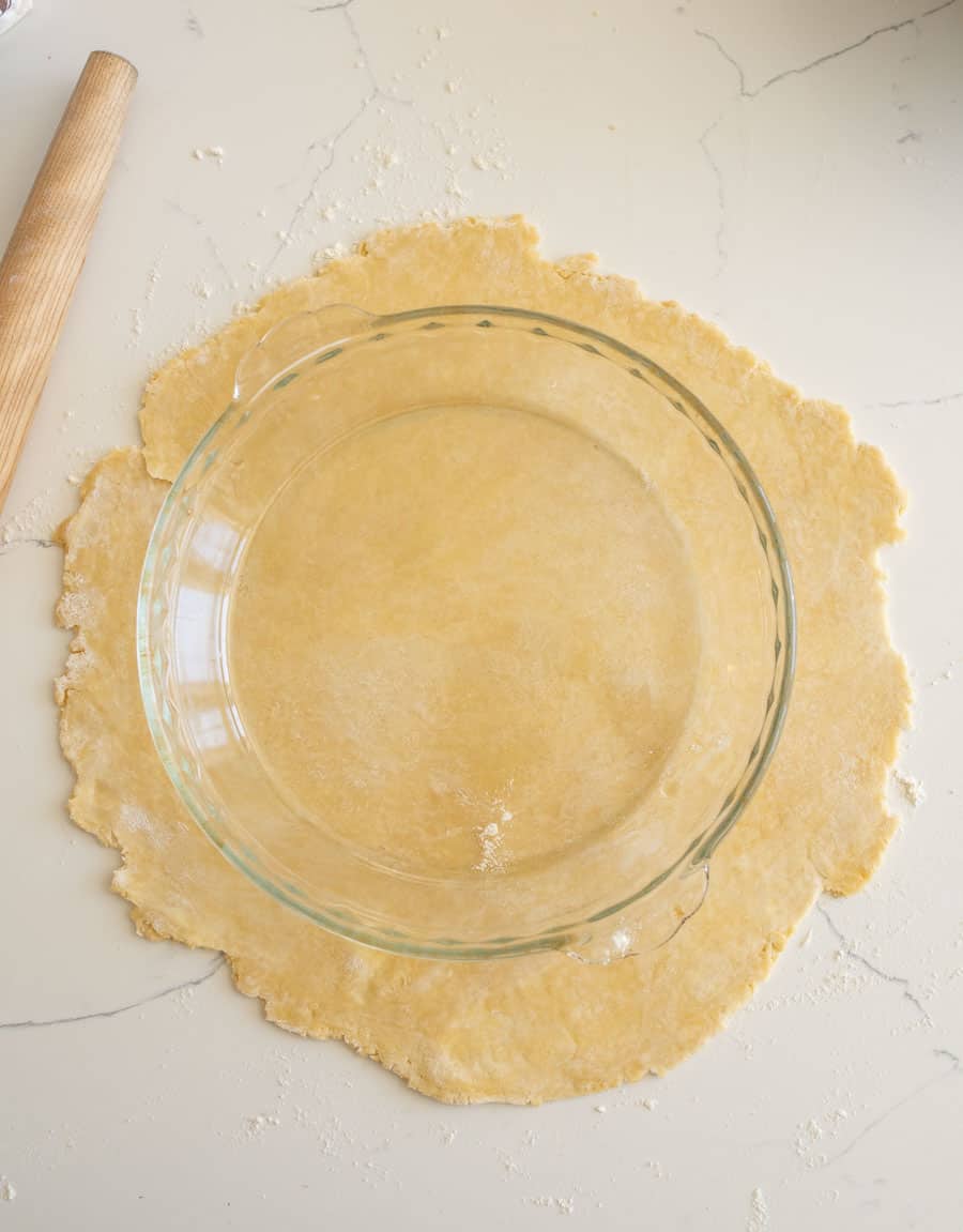 A pie plate placed on top of a rolled out pie crust to check the size of the crust on a white counter. 