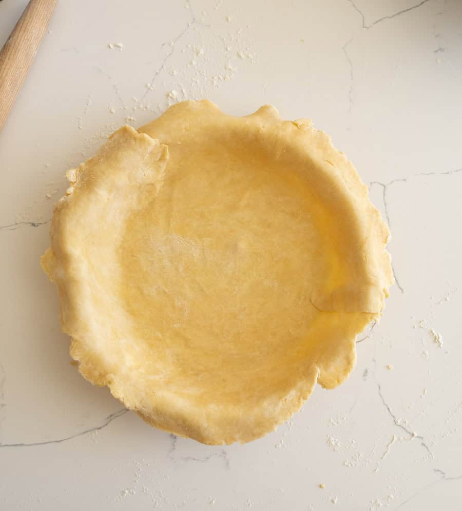 The pie crust unfolded into the clear glass pie plate on a white counter. 