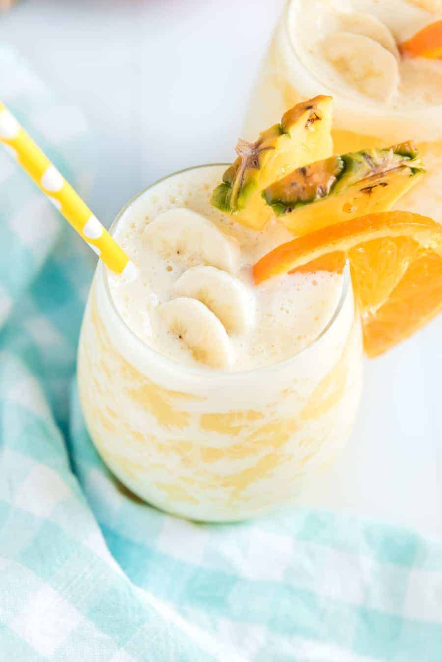 orange pineapple banana smoothie in a glass with a yellow straw.
