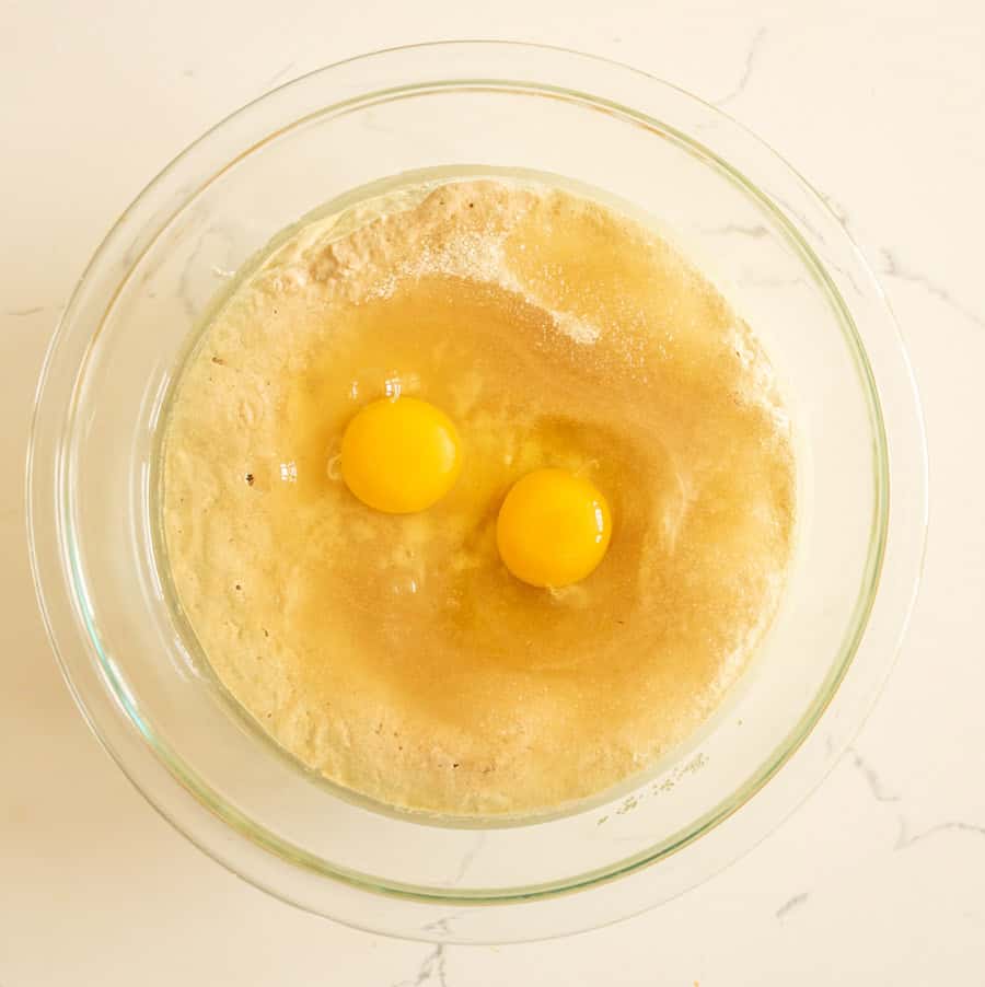 Sourdough muffin batter in a clear glass bowl with two eggs added. 