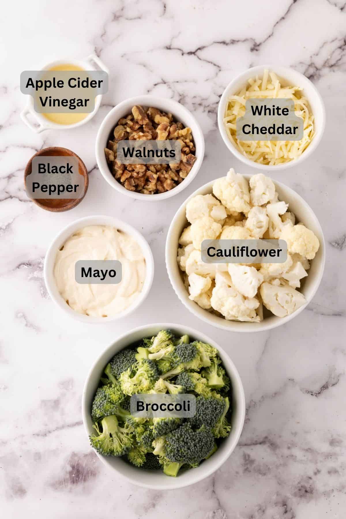 portion bowls each with digitally labeled raw ingredients to make broccoli cauliflower salad.