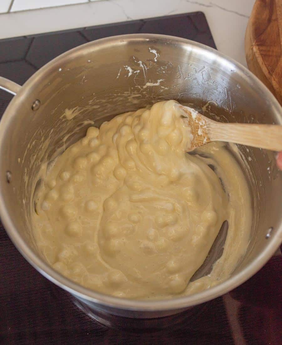 A pan on a stovetop with with the butter and marshmallow mixture being stirred with a wooden spoon. 