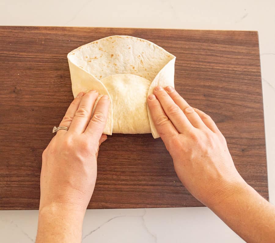 Flour tortilla being folded tightly around the burrito filling. 