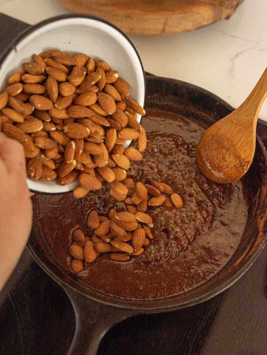 Almonds being added to the sugary mixture in a cat iron pan. 