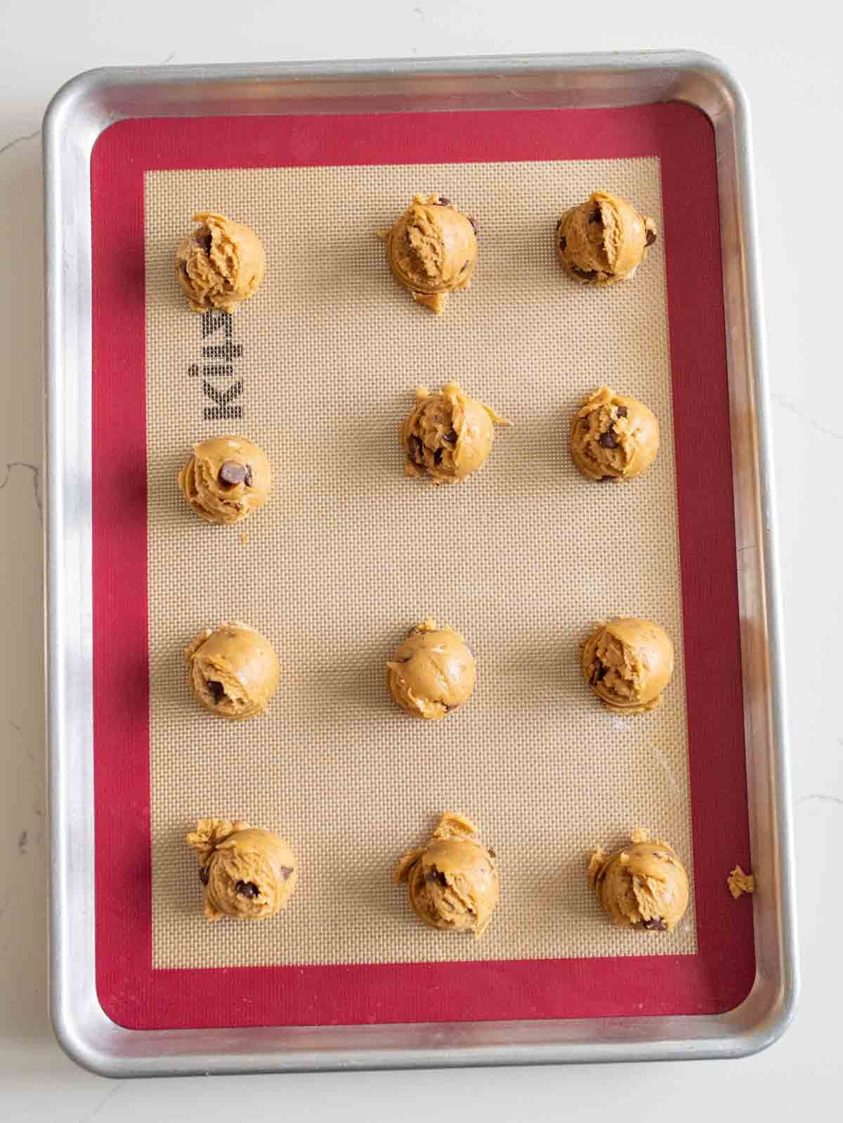 chocolate chip cookies with peanut butter chips dough balls rolled out onto the baking sheet.