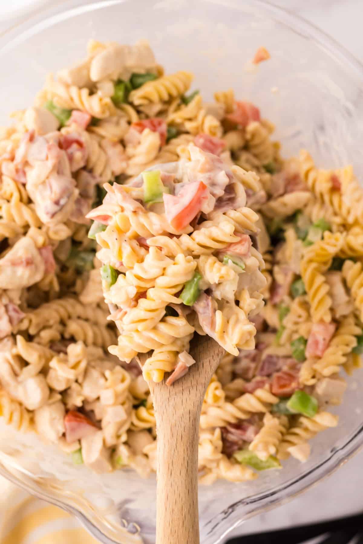 Creamy chicken bacon pasta in a clear mixing bowl with a wooden spoon.