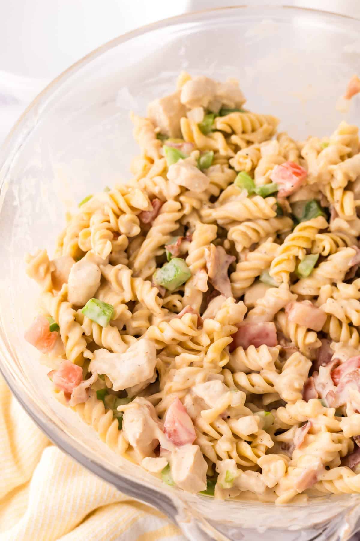 Creamy chicken bacon pasta in a clear mixing bowl.
