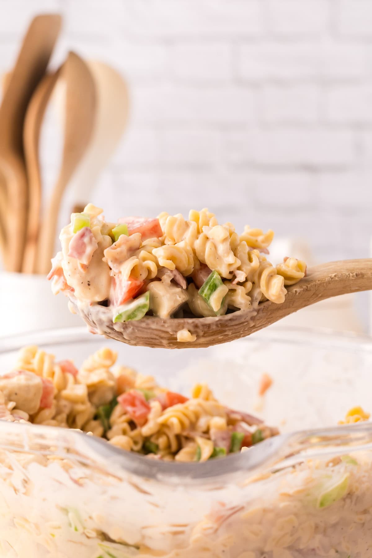 Creamy chicken bacon pasta in a clear mixing bowl with a wooden spoon.