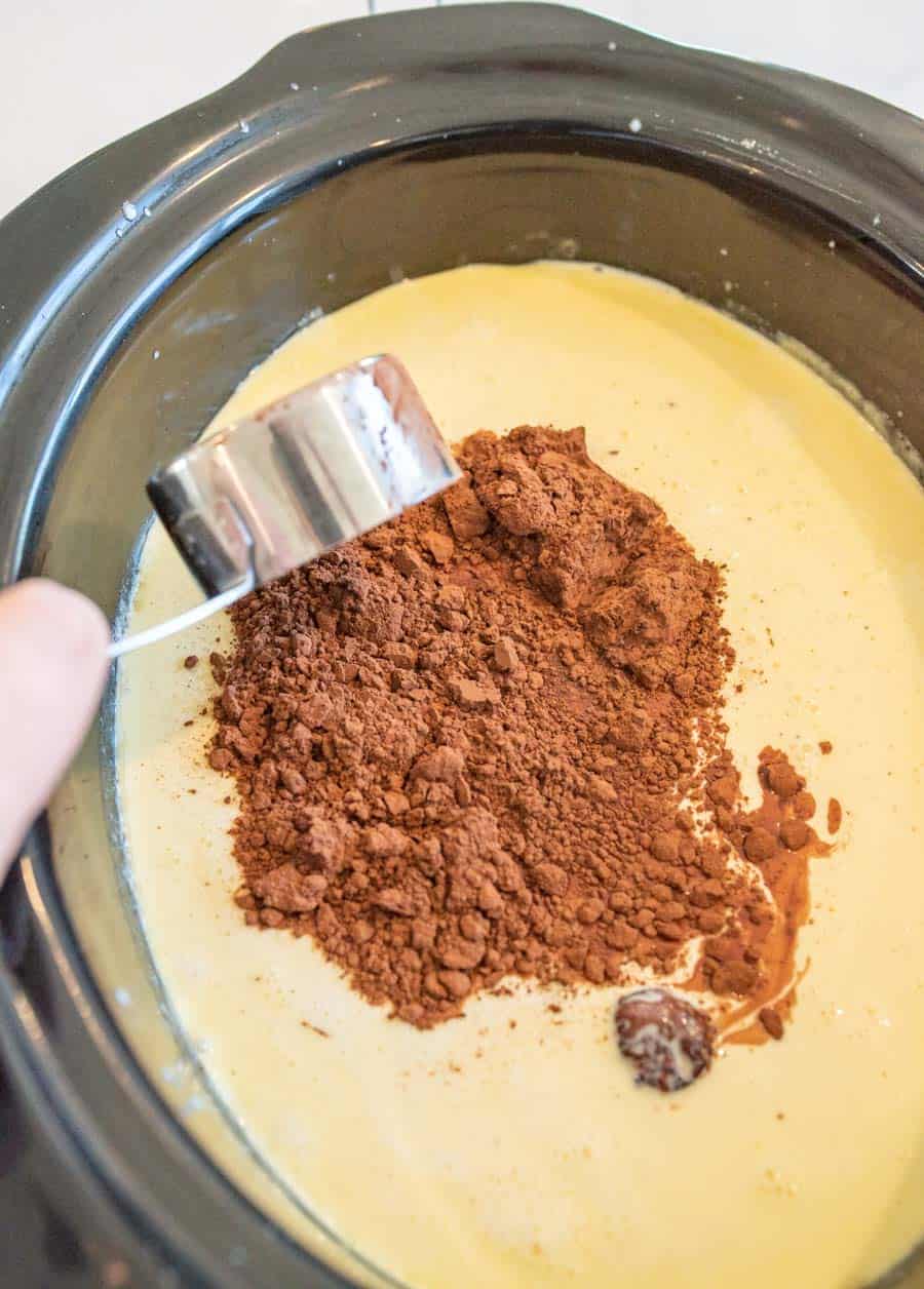 Cocoa powder being added to the crock pot with milk, cream, and sweetened condensed milk. 