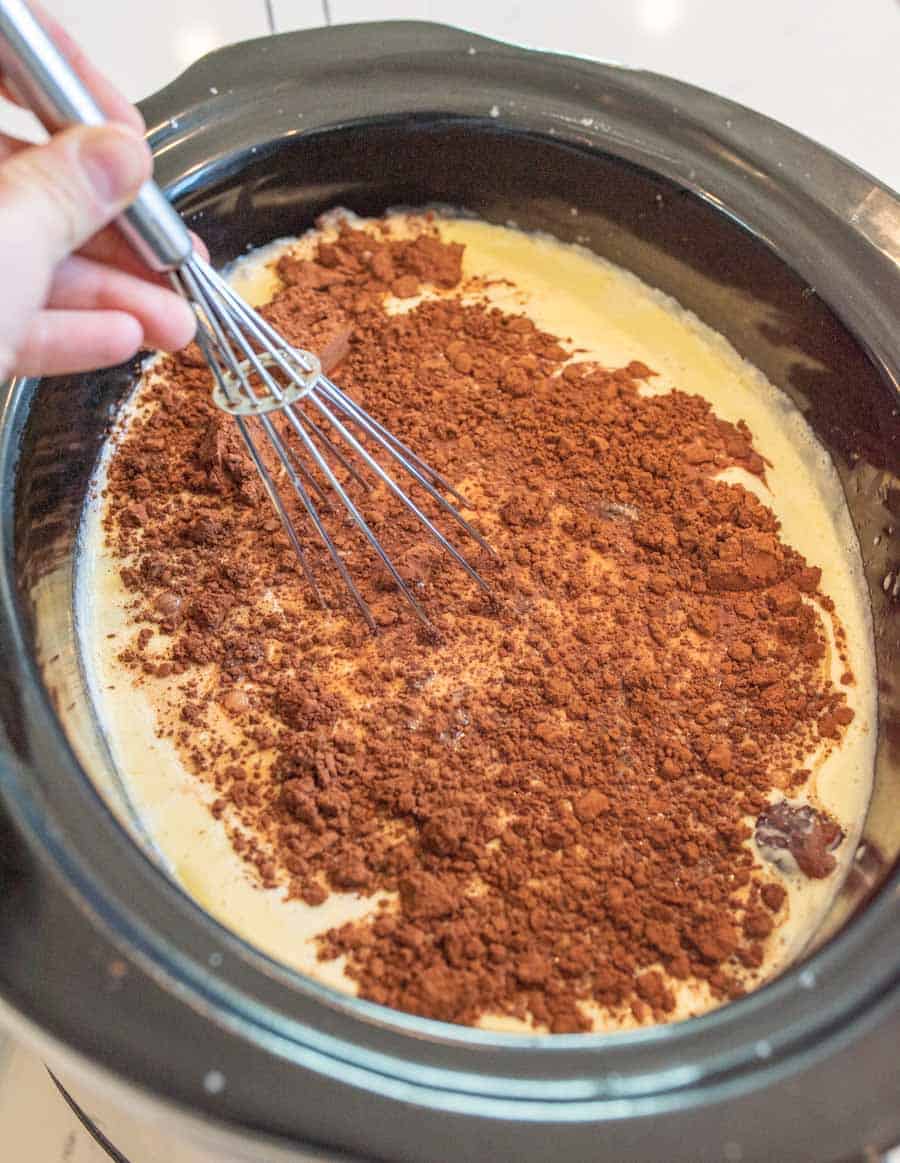 Cocoa powder and chocolate chips being whisked into the hot milk mixture in the crock pot. 