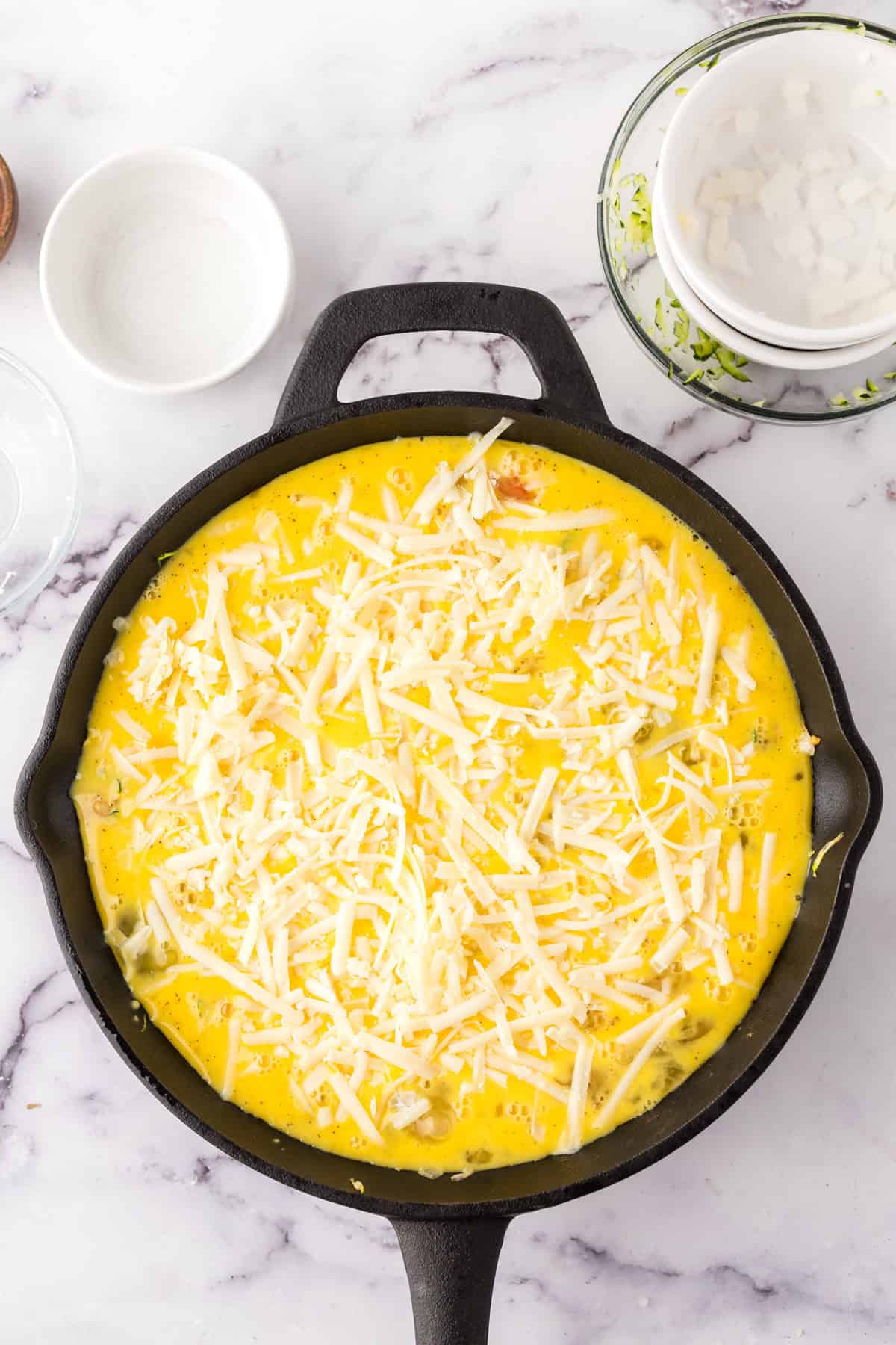 Farmhouse egg bake recipe whole in a cast iron pan with cheese on top before baking.