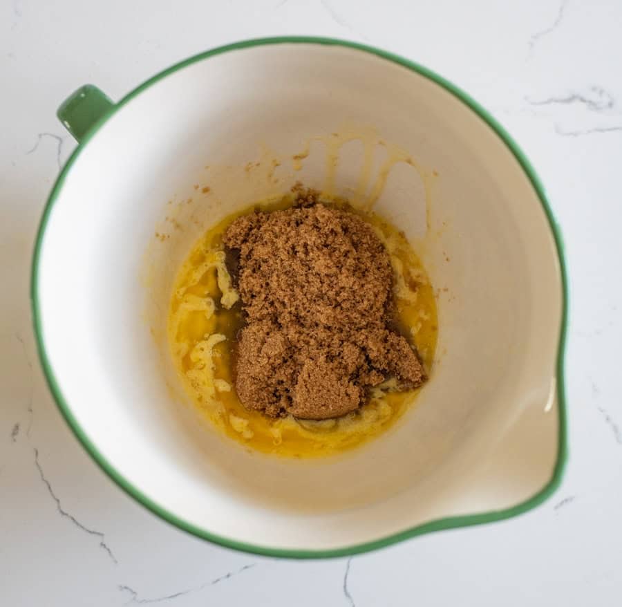 Butter and brown sugar in a white bowl with a green rim on a white counter. 