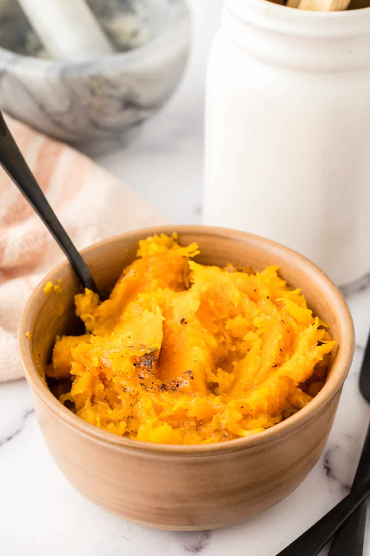 baked soft and smashed butternut squash in a small bowl with a black fork.