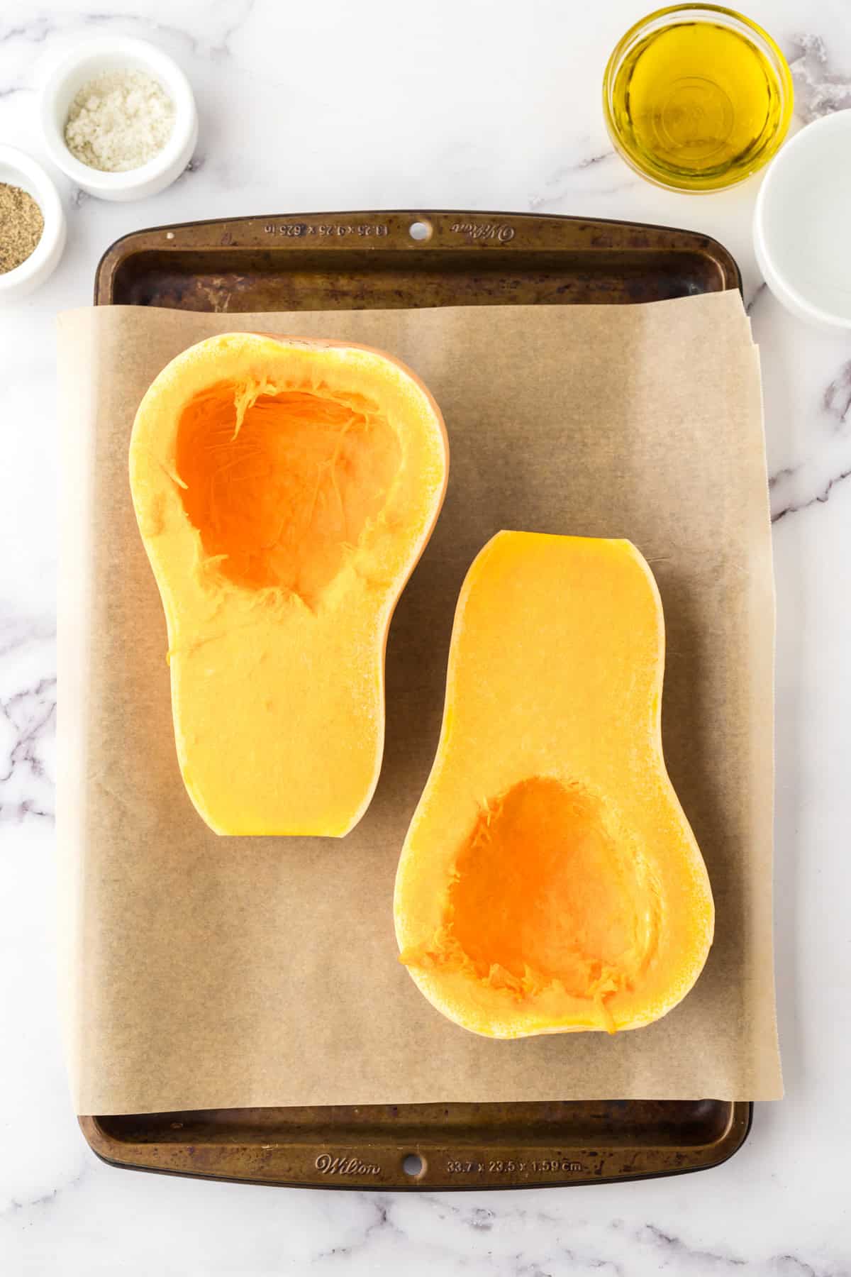 how to bake butternut squash showing the halved squash on parchment over a baking sheet.