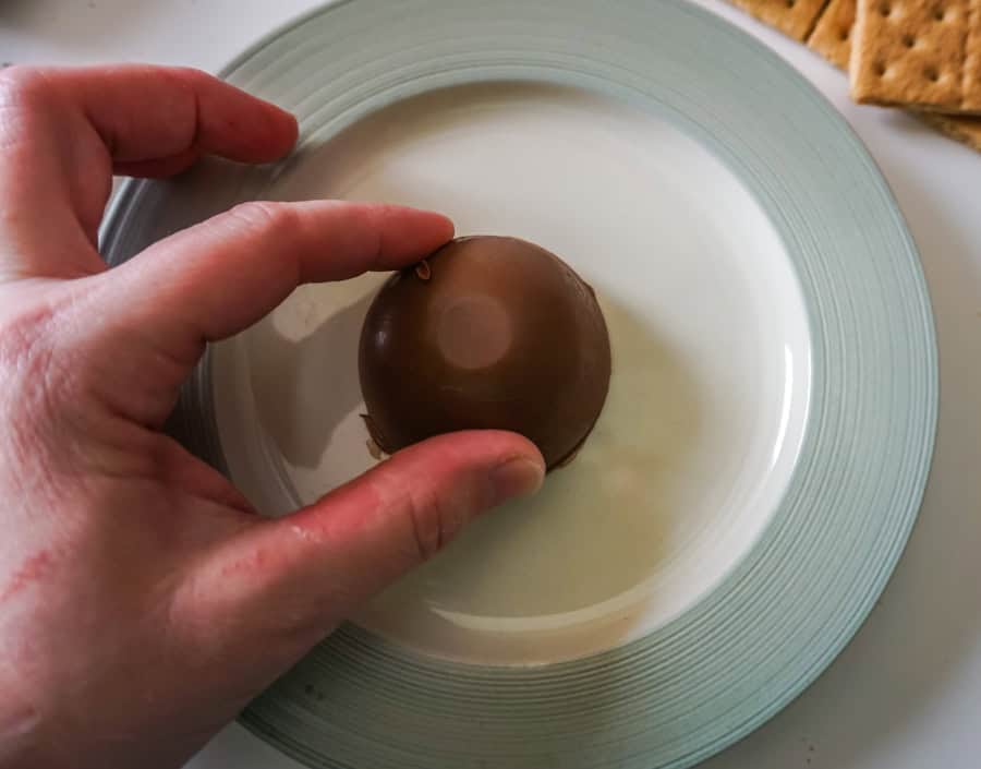 A hand rubbing half of a chocolate bomb on a warm plate. 