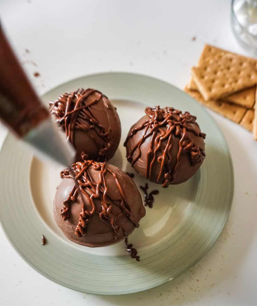 Melted chocolate being drizzled on the top of three completed hot chocolate bombs. 