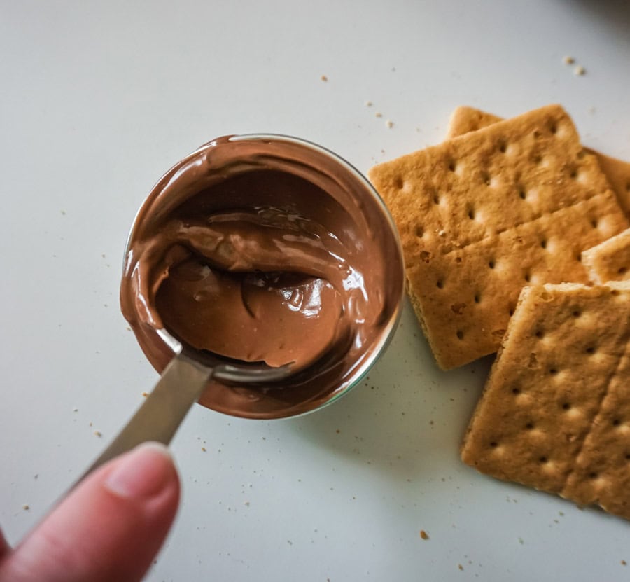 A tablespoon spreading melted chocolate in a mold with graham crackers in the background. 