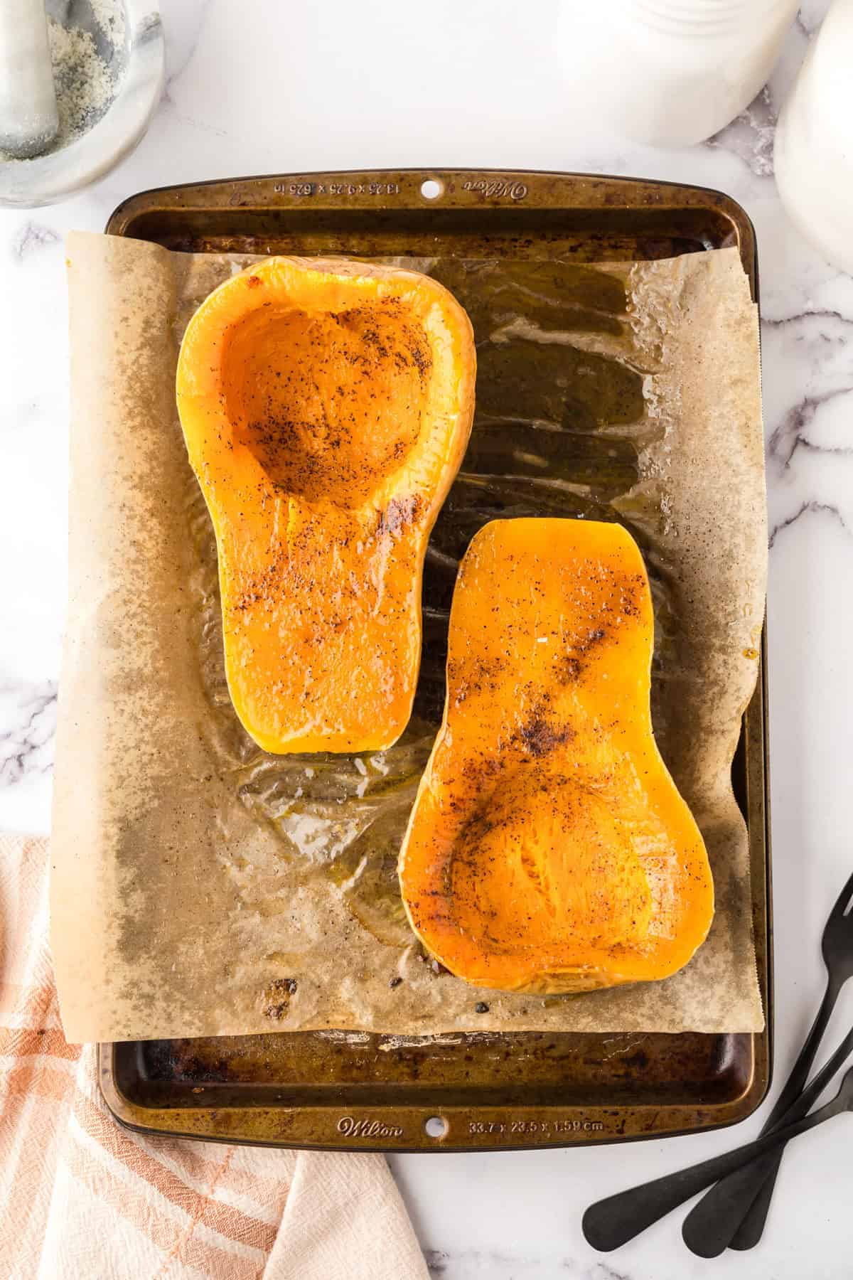 how to bake butternut squash showing the halved squash on parchment over a baking sheet seasoned and baked.