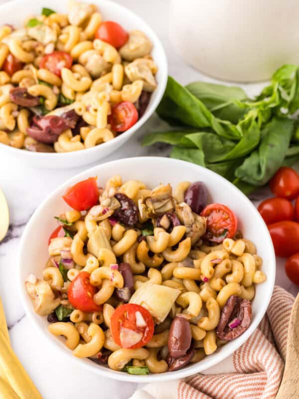 two white bowls of Italian Pasta Salad Recipe with whole cherry tomatoes and golden spoons to the side.