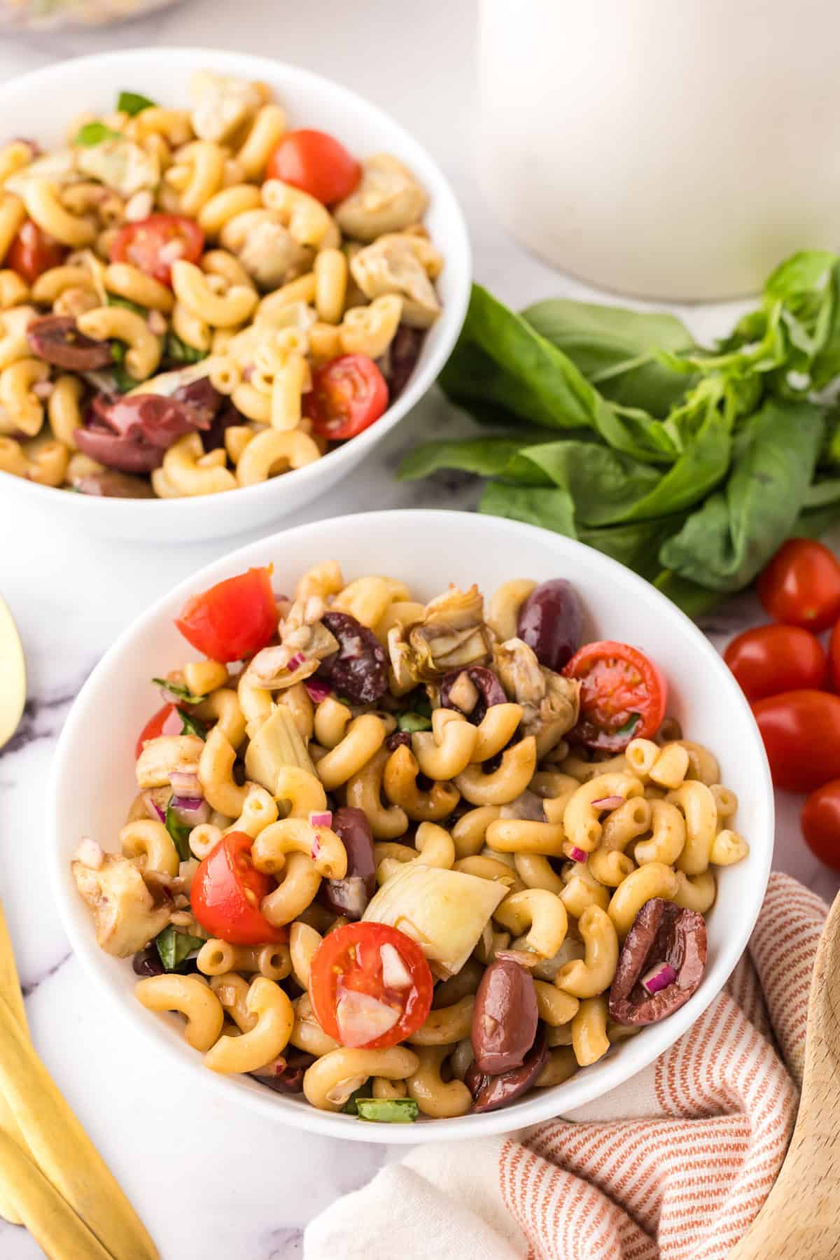 two white bowls of Italian Pasta Salad Recipe with whole cherry tomatoes and golden spoons to the side.