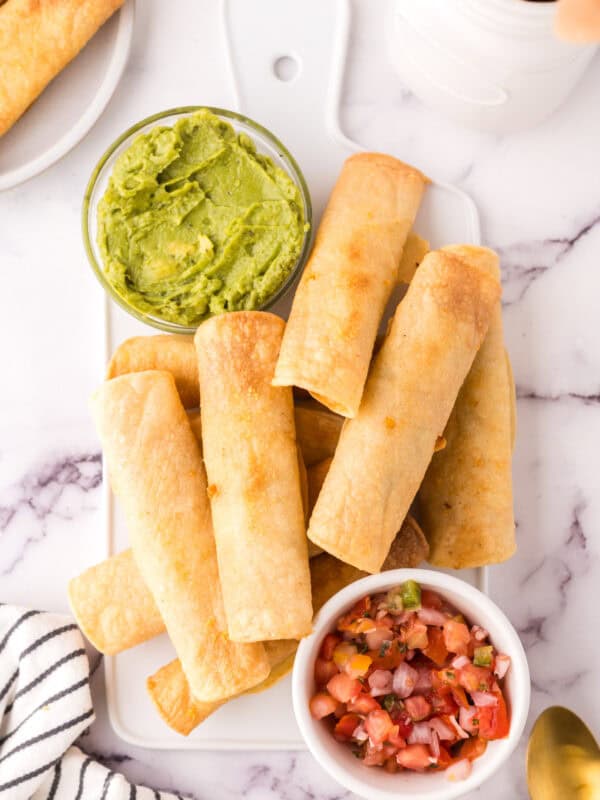 pile of taquitos on a plate with guacamole and salsa.