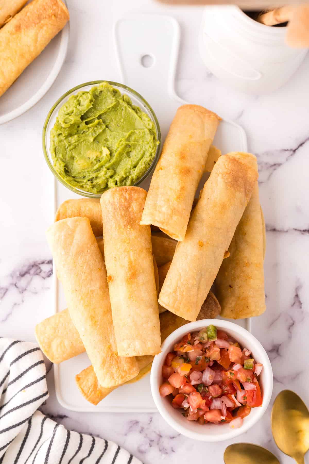 pile of taquitos on a plate with guacamole and salsa. 